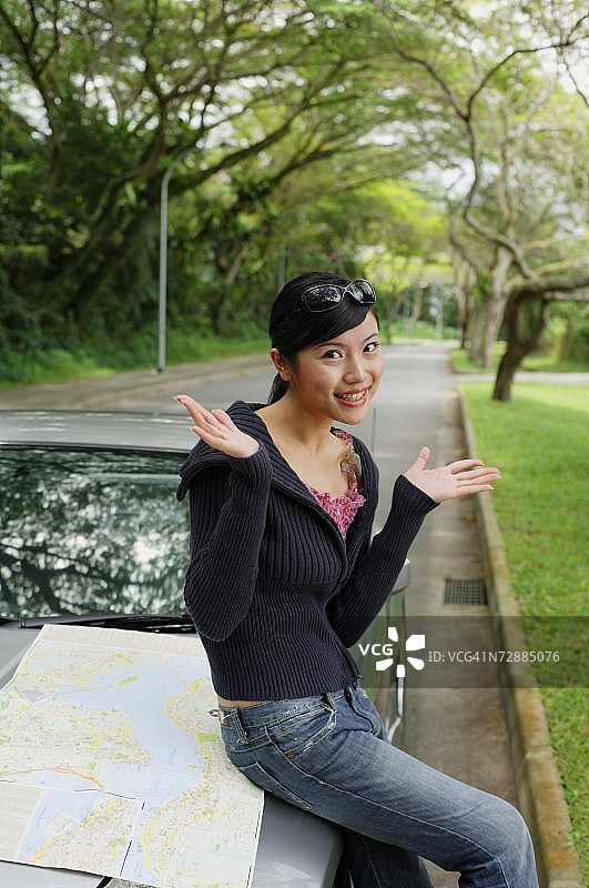 坐在汽车引擎盖上，旁边放着地图，举起双手的女人图片素材