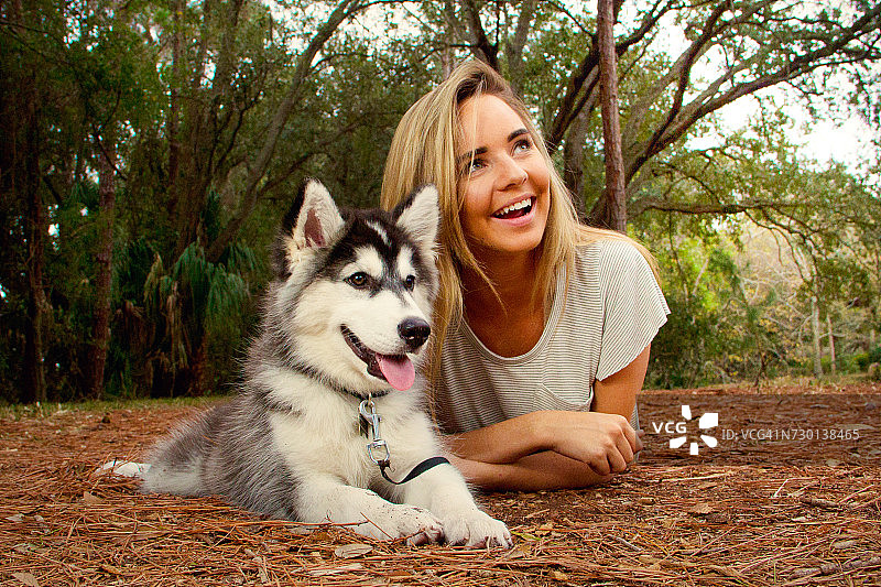 女人躺在地上，旁边是西伯利亚哈士奇幼犬，美国佛罗里达州圣彼得堡图片素材