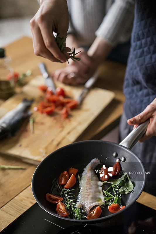 年轻夫妇在厨房灶台上用香草煎鱼图片素材