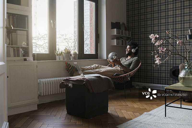 男人坐在客厅的扶手椅上，拿着镜面球听音乐图片素材