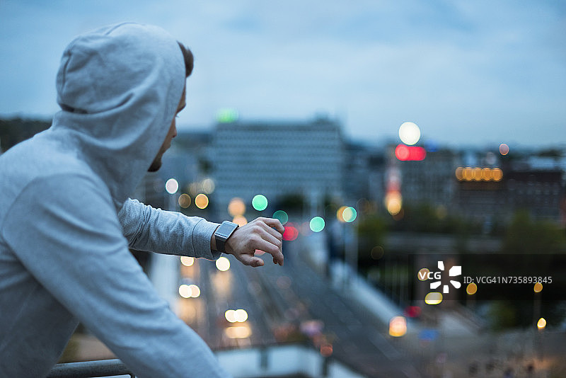 运动员在黎明时分于城市上方查看智能手表图片素材