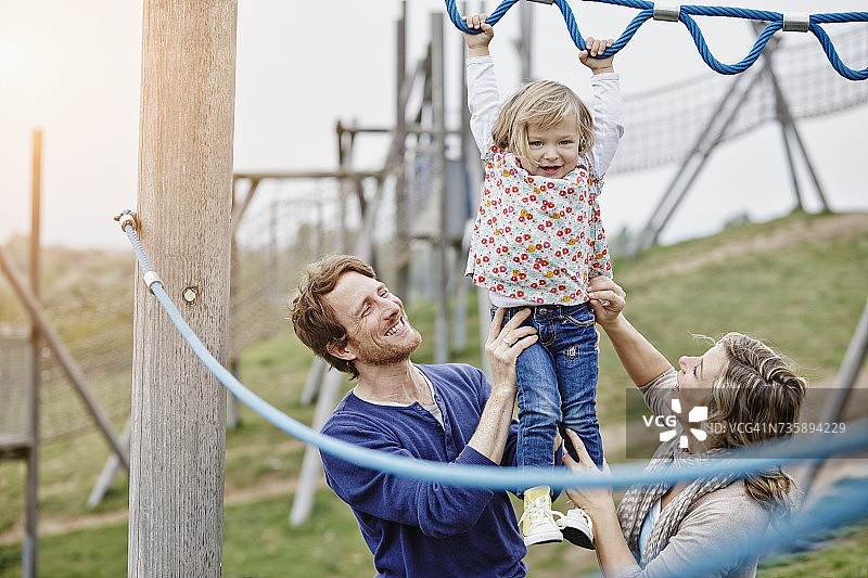 在游乐场攀爬网上，由父母支持的女孩图片素材