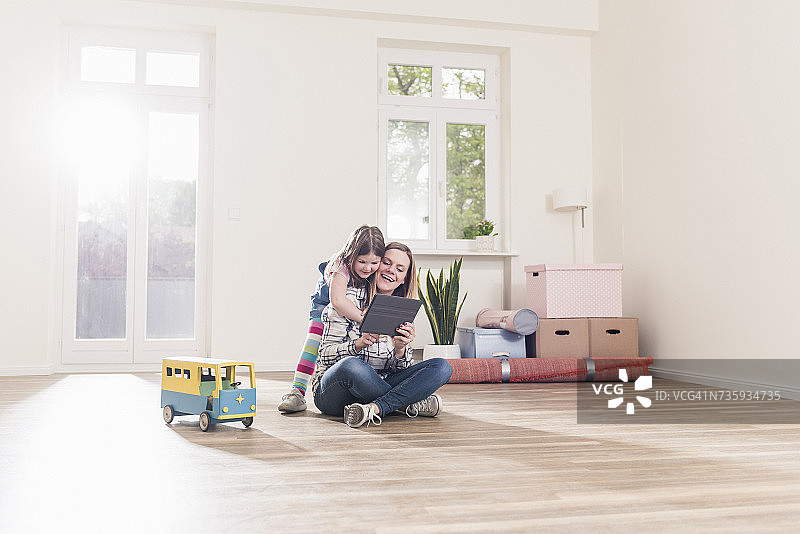 快乐的女孩和母亲在空公寓里使用平板电脑图片素材