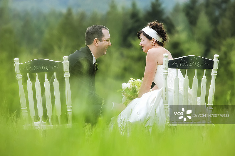 新娘和新郎并排坐在草地上的椅子上，边交谈边欢笑图片素材