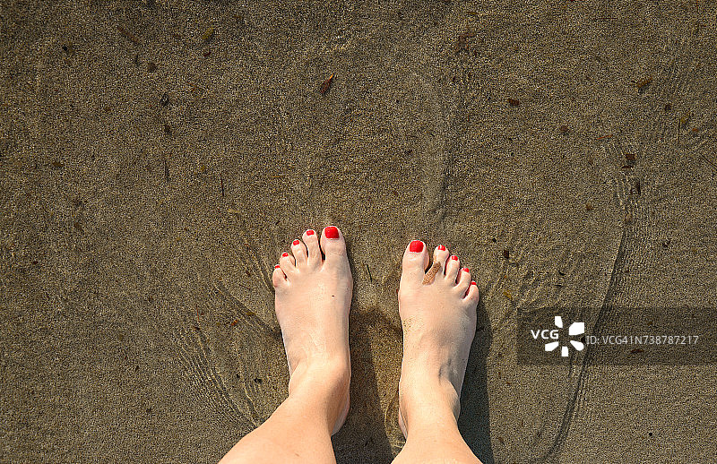 女士涂有指甲油的双脚站在沙滩湿沙上图片素材