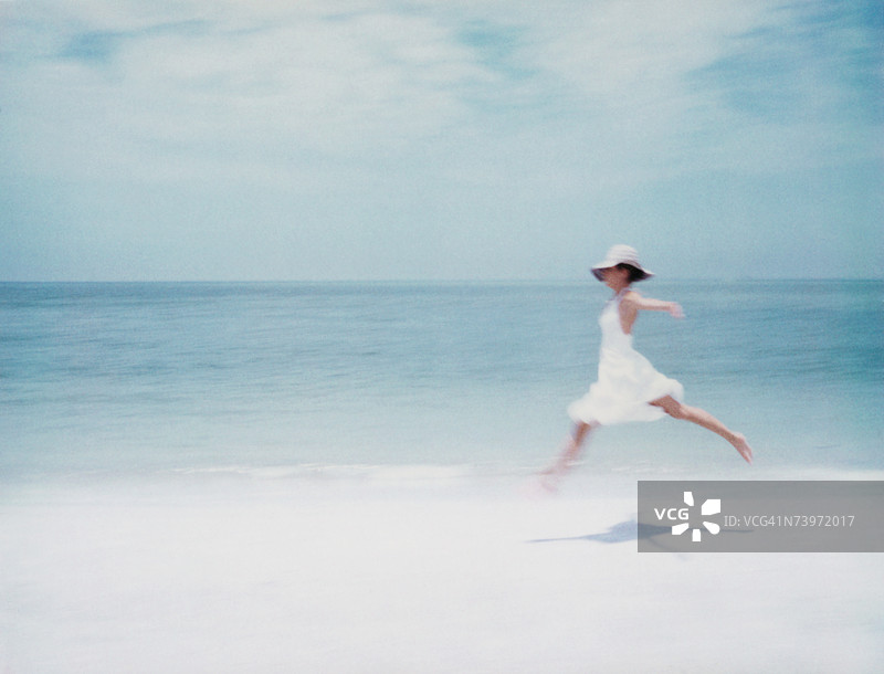 穿着裙子的年轻女性在海滩上跳跃，双臂张开，侧面视角图片素材