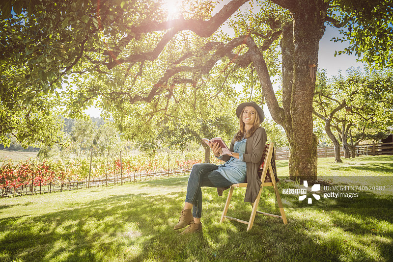 西班牙裔妇女坐在椅子上在树下读书图片素材