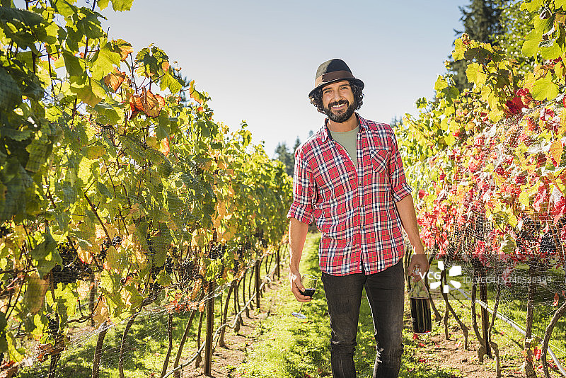 在葡萄园里手持葡萄酒的西班牙裔男人图片素材