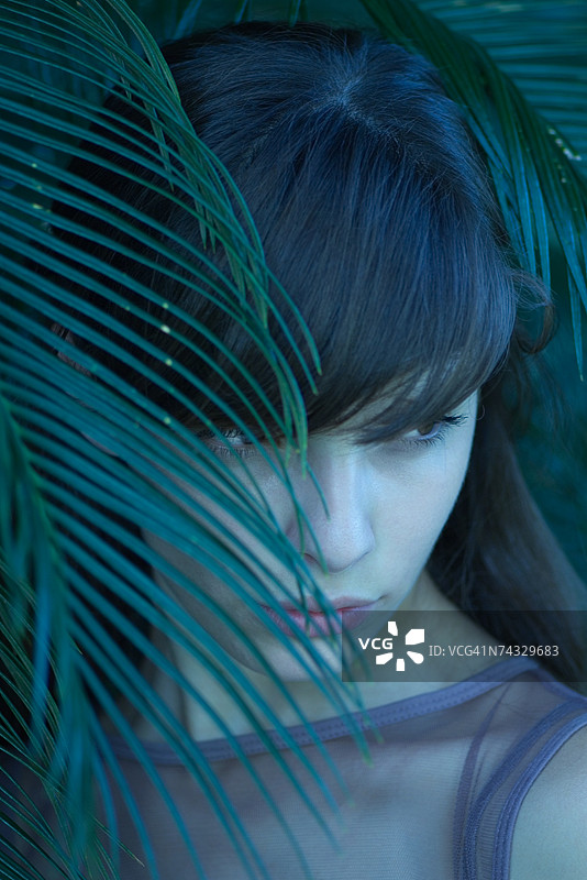 女人站在树叶后面，望向远方图片素材