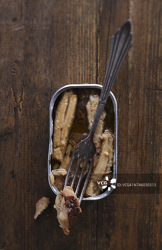 木桌上放着一罐打开的沙丁鱼罐头和叉子图片素材