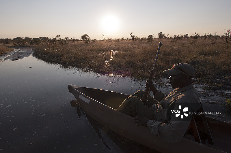 在博茨瓦纳奥卡万戈三角洲，划独木舟持步枪的男人图片素材
