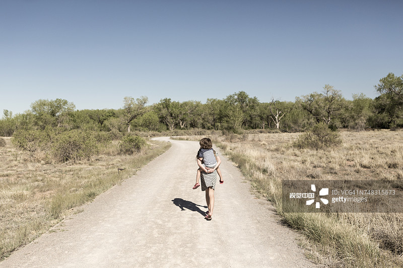 白人女孩在泥泞小路上背着弟弟图片素材