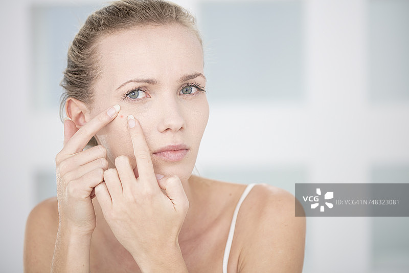 年轻女子照镜子，准备挤痘痘图片素材