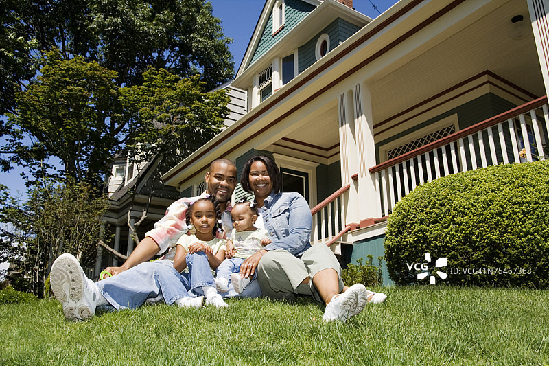 一对年轻的非裔美国家庭坐在郊区家园前的草地上。图片素材