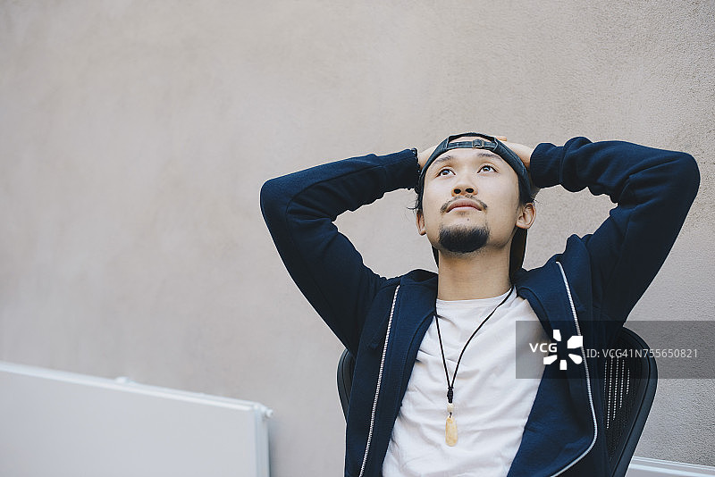 在办公室里双手放在头后，对着米色墙壁沉思的男程序员图片素材