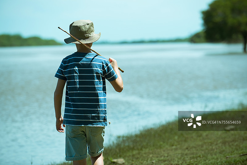 男孩拿着钓鱼竿在湖边行走（背影）图片素材