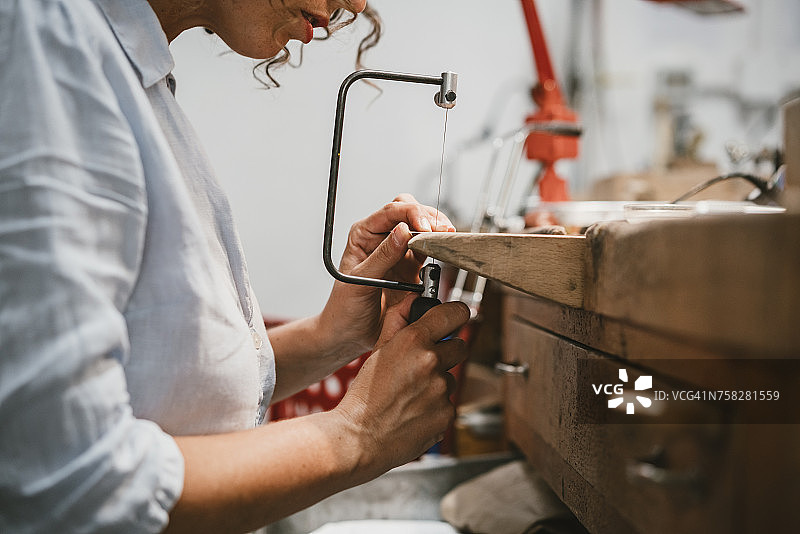 女珠宝商在工作台上使用钢丝锯的局部图图片素材
