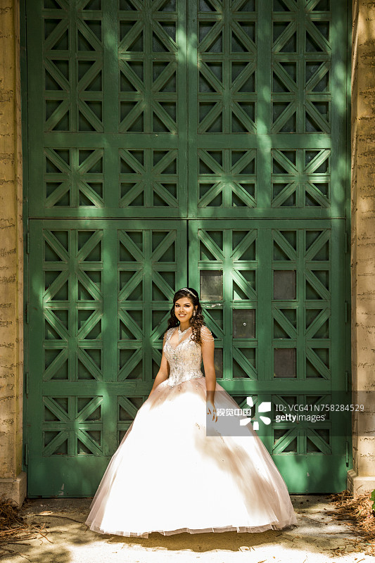 微笑的西班牙裔女孩穿着礼服靠近绿色的墙壁图片素材