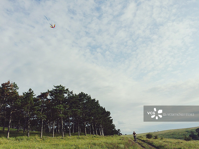 男人在人行道上骑自行车，天空中飘着风筝图片素材