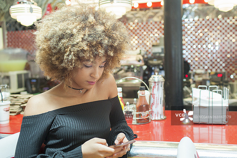 年轻女人坐在餐馆里，看着智能手机图片素材