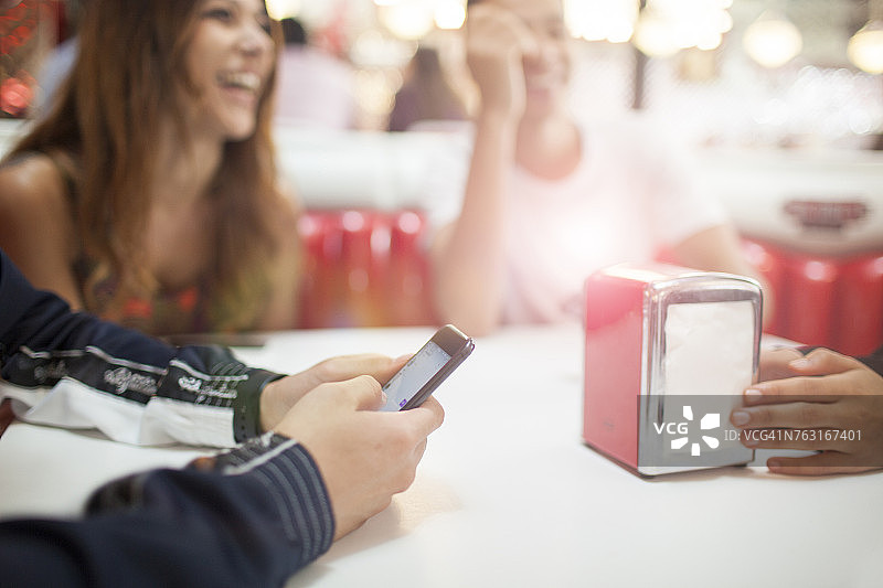 一群年轻朋友在餐厅就座，一名年轻男子正在使用智能手机图片素材