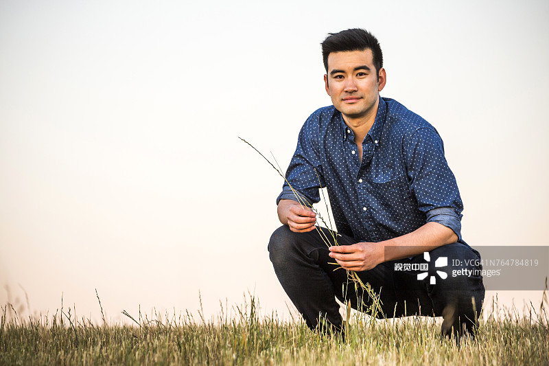 蹲在田野里拿着草的中国男人图片素材