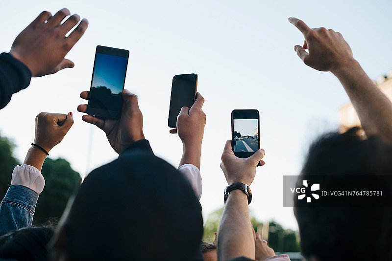 低角度拍摄：朋友们用智能手机对着天空拍照图片素材