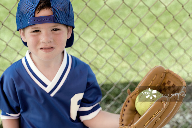 穿着棒球服、戴着手套站在栅栏边的男孩图片素材