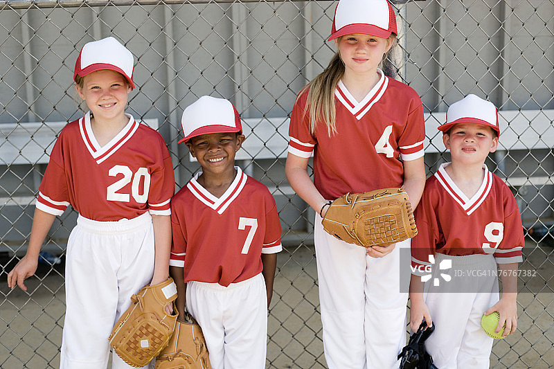 孩子们身穿棒球服，戴着手套站在栅栏旁图片素材