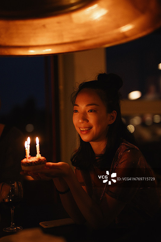 快乐的女人在暗室里拿着带蜡烛的小生日蛋糕图片素材