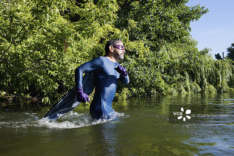 在河里奔跑的成熟超级英雄的侧视图，背景是树木图片素材