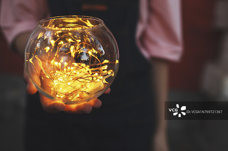 少女手捧玻璃碗中发光灯串的局部照片图片素材
