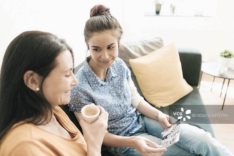 母亲和成年女儿坐在家里的沙发上看照片图片素材