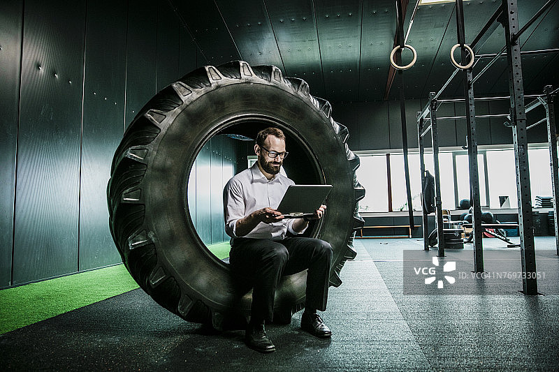 坐在健身房卡车轮胎上使用笔记本电脑的商人图片素材