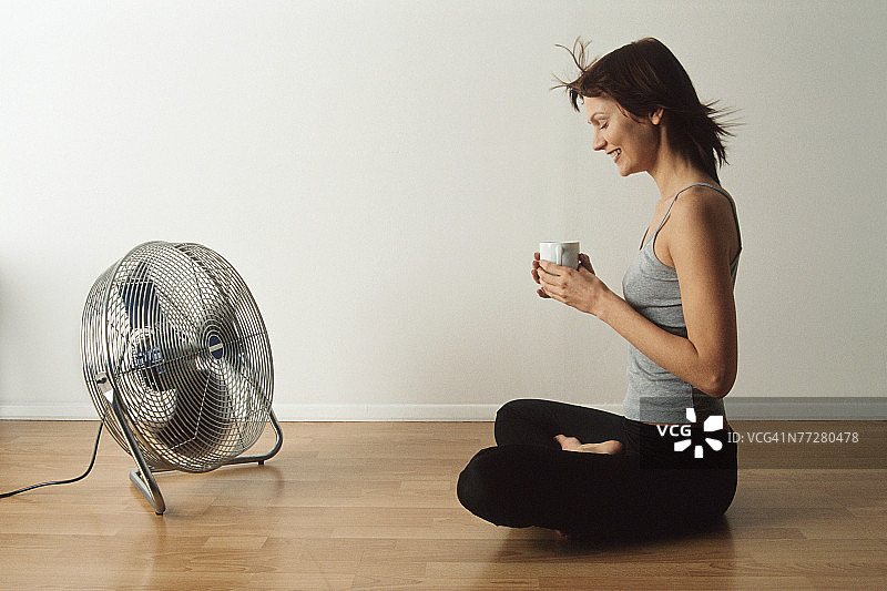 女人坐在地板上，面前放着一个风扇图片素材