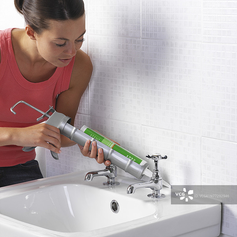 女士在墙壁和水槽之间涂抹密封胶图片素材