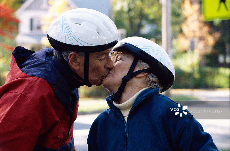 一对成熟的白人异性恋夫妇戴着自行车头盔接吻。图片素材