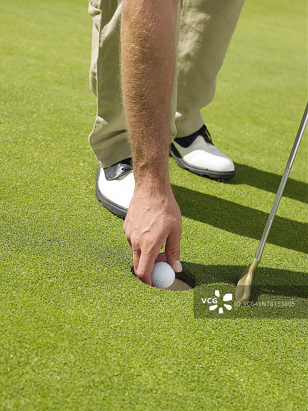 男子从高尔夫球洞中取出高尔夫球图片素材