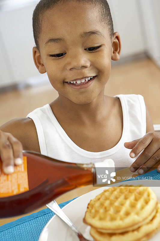 男孩在华夫饼上倒糖浆图片素材