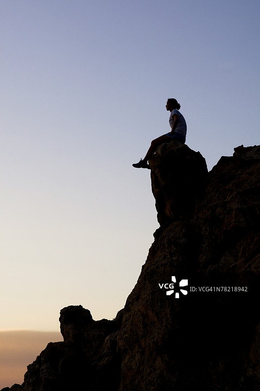 女人坐在黄昏时分的悬崖顶端图片素材