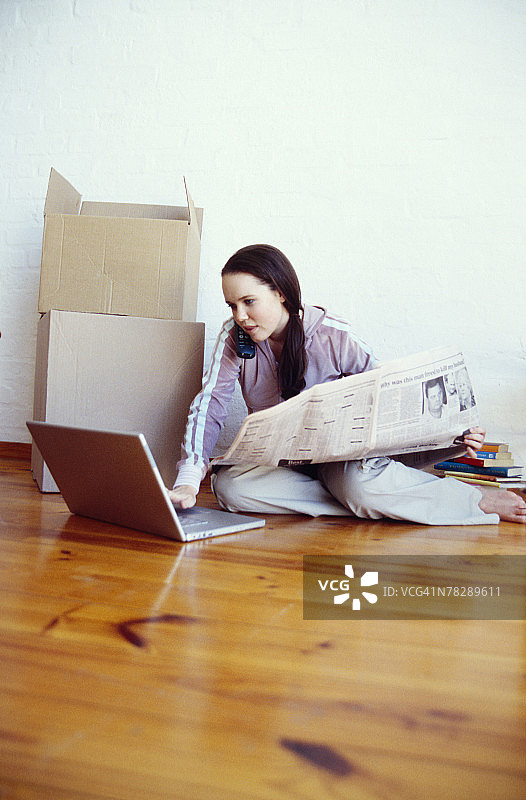坐在地板上看报纸用笔记本电脑的女人图片素材