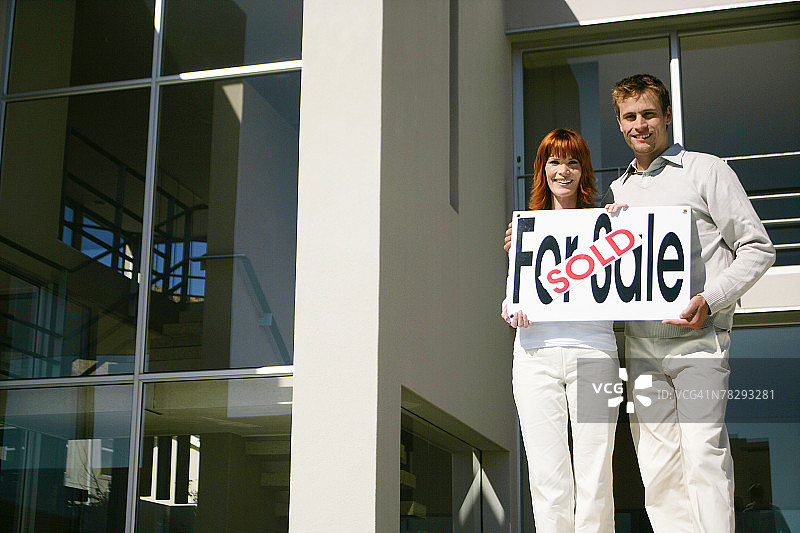 情侣在新房旁拿着已售标志图片素材