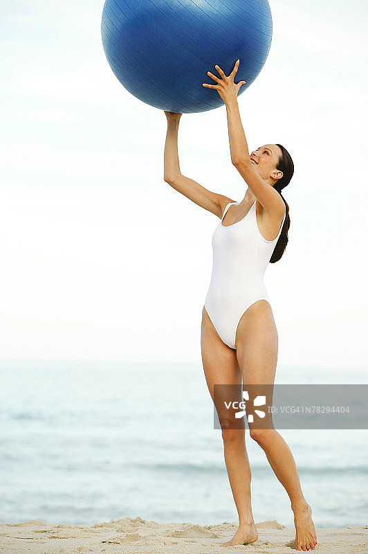 在海滩上举着健身球的女人图片素材