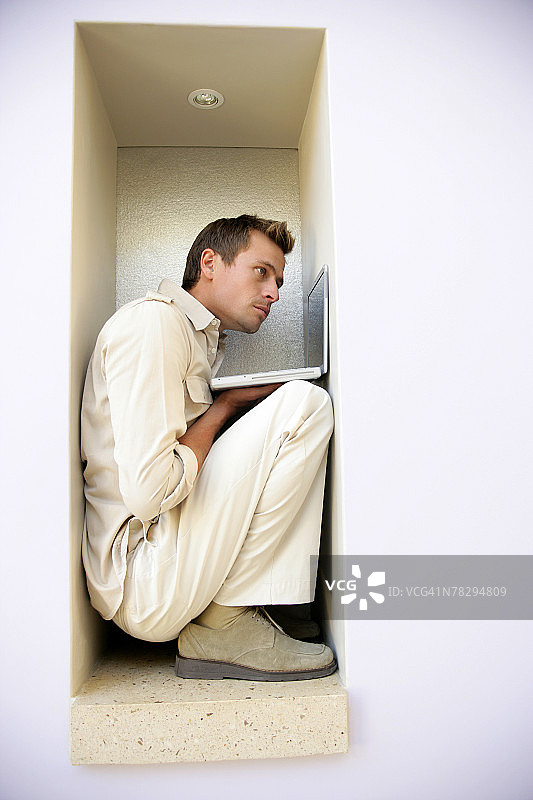 狭窄空间里使用笔记本电脑的男人图片素材