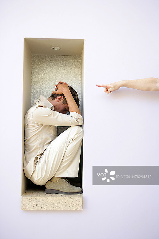 手指向坐在狭窄空间里畏缩的男人图片素材