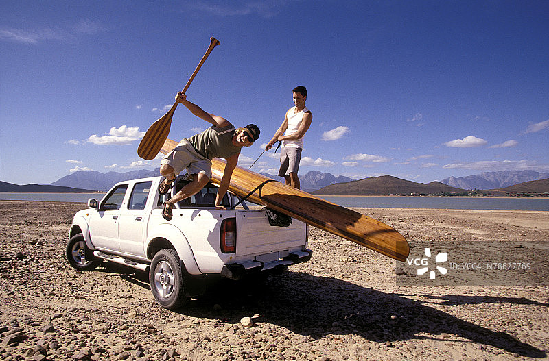 男士在干旱的海滩上将独木舟装载到卡车上图片素材