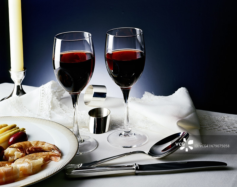 两杯葡萄酒旁边放着一盘虾。图片素材