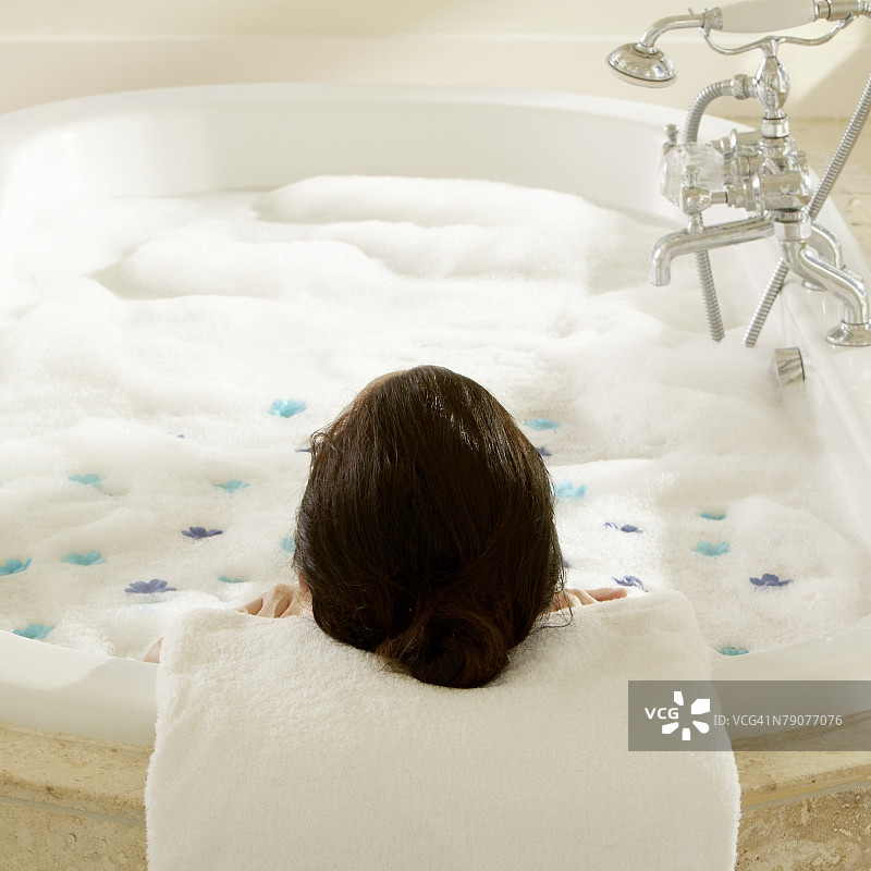 高角度拍摄：在撒满花瓣的泡泡浴缸中沐浴的女人图片素材