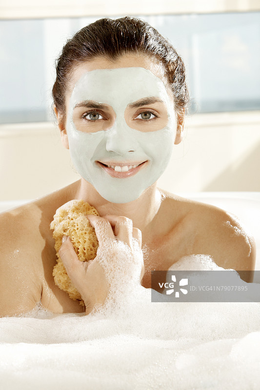 敷着面膜、拿着沐浴海绵微笑的年轻女子肖像图片素材