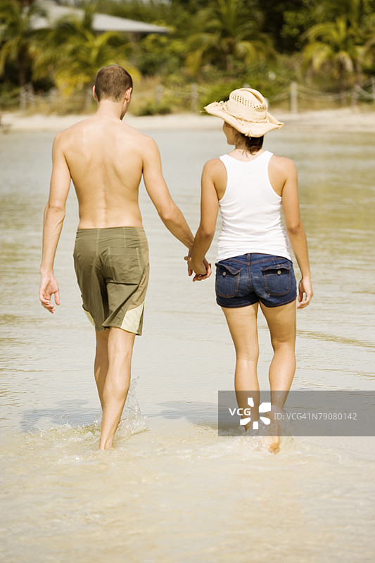 年轻男孩和少女手牵手在海滩上散步的背影图片素材